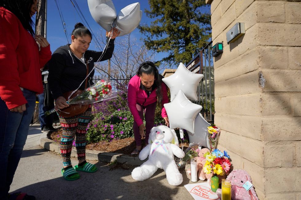 Ana DeJesus, right, places a teddy bear on a growing memorial at The Church in Sacramento, Calif., on Tuesday, March 1, 2022. At left, Vera Cruz waits to leave flowers and balloons. Authorities say a man shot and killed his three daughters, their chaperone and himself during a supervised visit with the girls at the church on Monday.