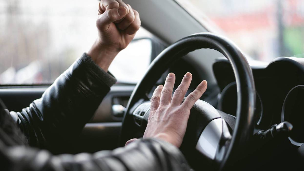 Angry driver is honking and is yelling by sitting of a steering wheel. Road aggression concept. Traffic jam.