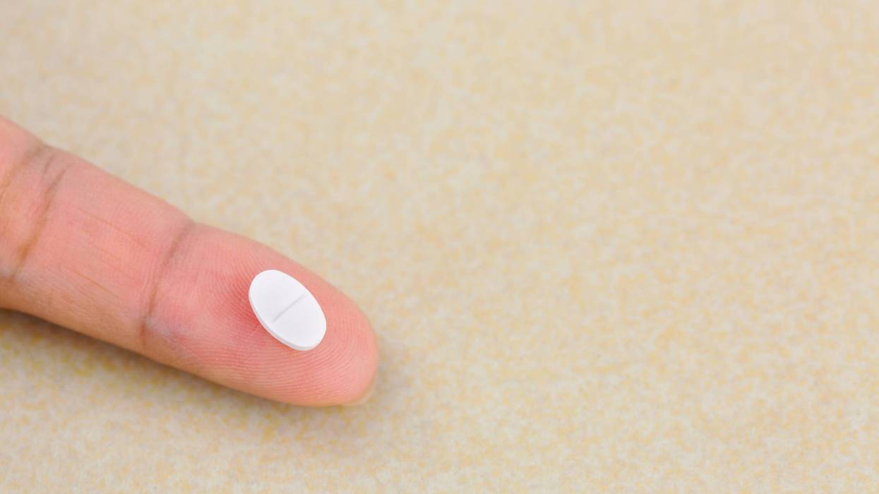 Anti anxiety white pill medicine on finger with blurred yellow background