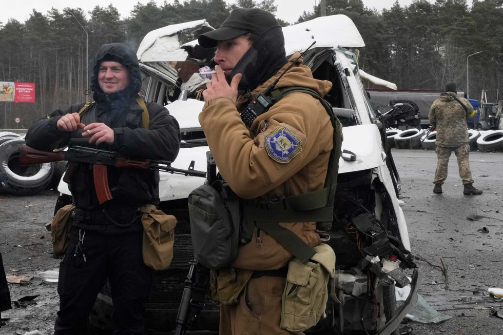 Armed men smoke by a damaged vehicle at a checkpoint in Brovary, outside Kyiv, Ukraine, Tuesday, March 1, 2022