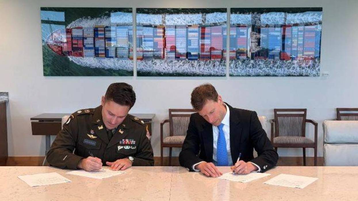 Army officer and businessman sign documents. Large cargo ship artwork on the wall.