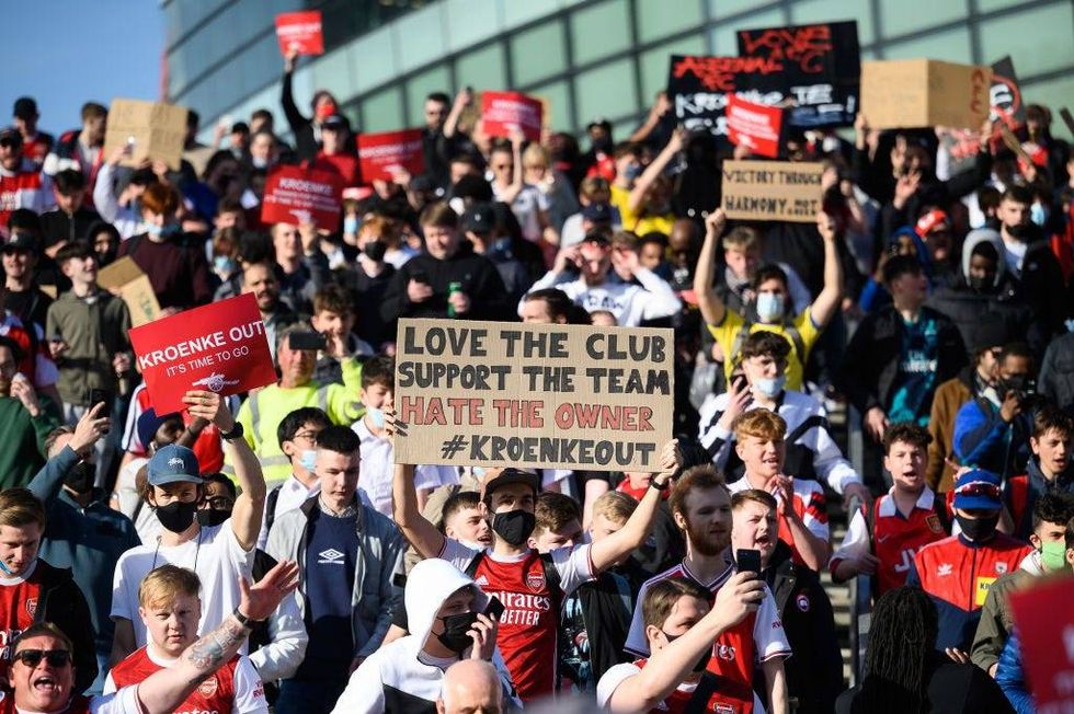 Arsenal fans chant and hold placards during a protest against the club
