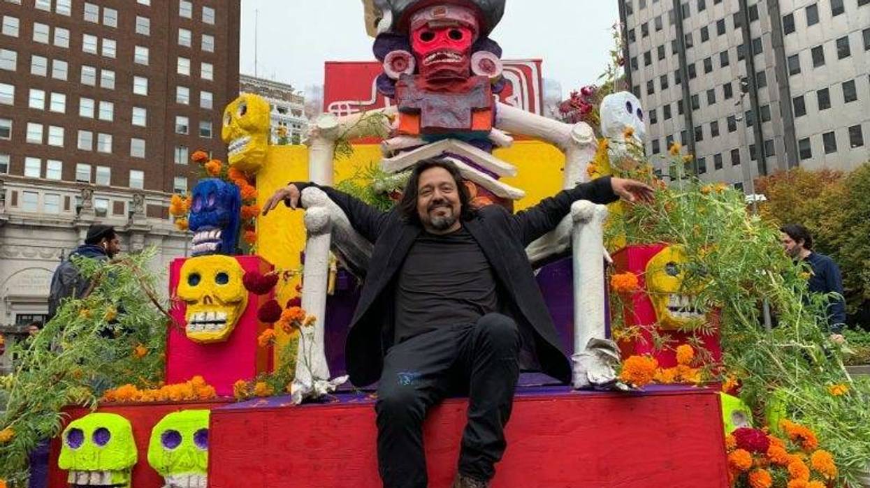 Artist Cesar Vivaros sitting on top of the Dia De Muertos altar he created that in Love Park.