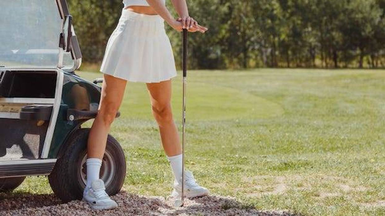 Attractive golfer woman posing in short skirt on course near golf cart