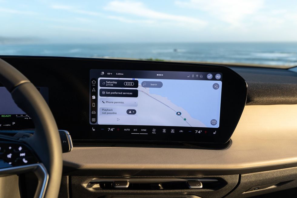 Audi car's infotainment screen shows navigation map, settings, and the ocean in the background.
