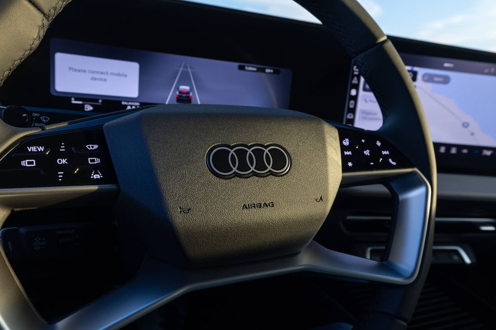 Audi steering wheel with multi-function controls and digital cockpit showing navigation and alerts.