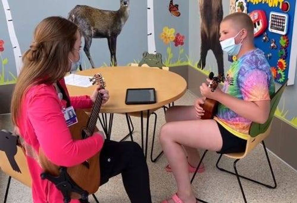 Ava and a hospital worker play guitar and ukulele in a children