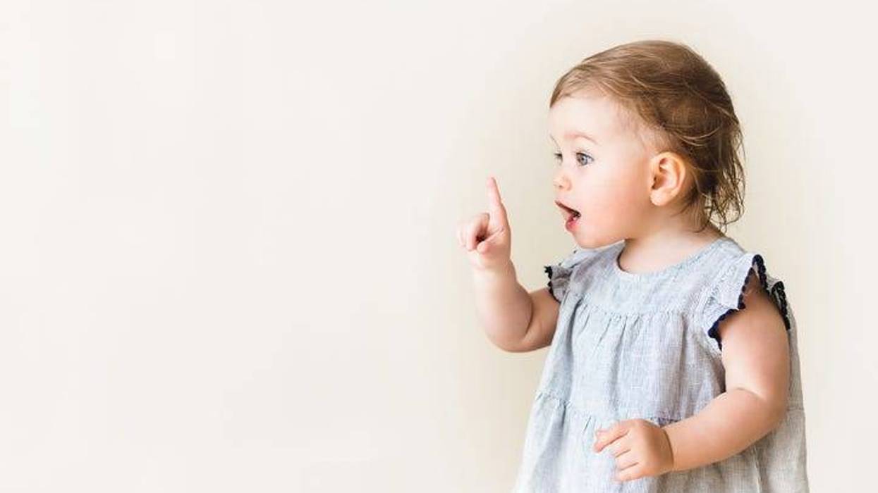 Baby girl pointing her finger, excited and emotional, on neutral background