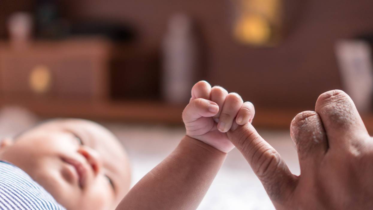 baby holding his parent's pinkie with his tiny little hand
