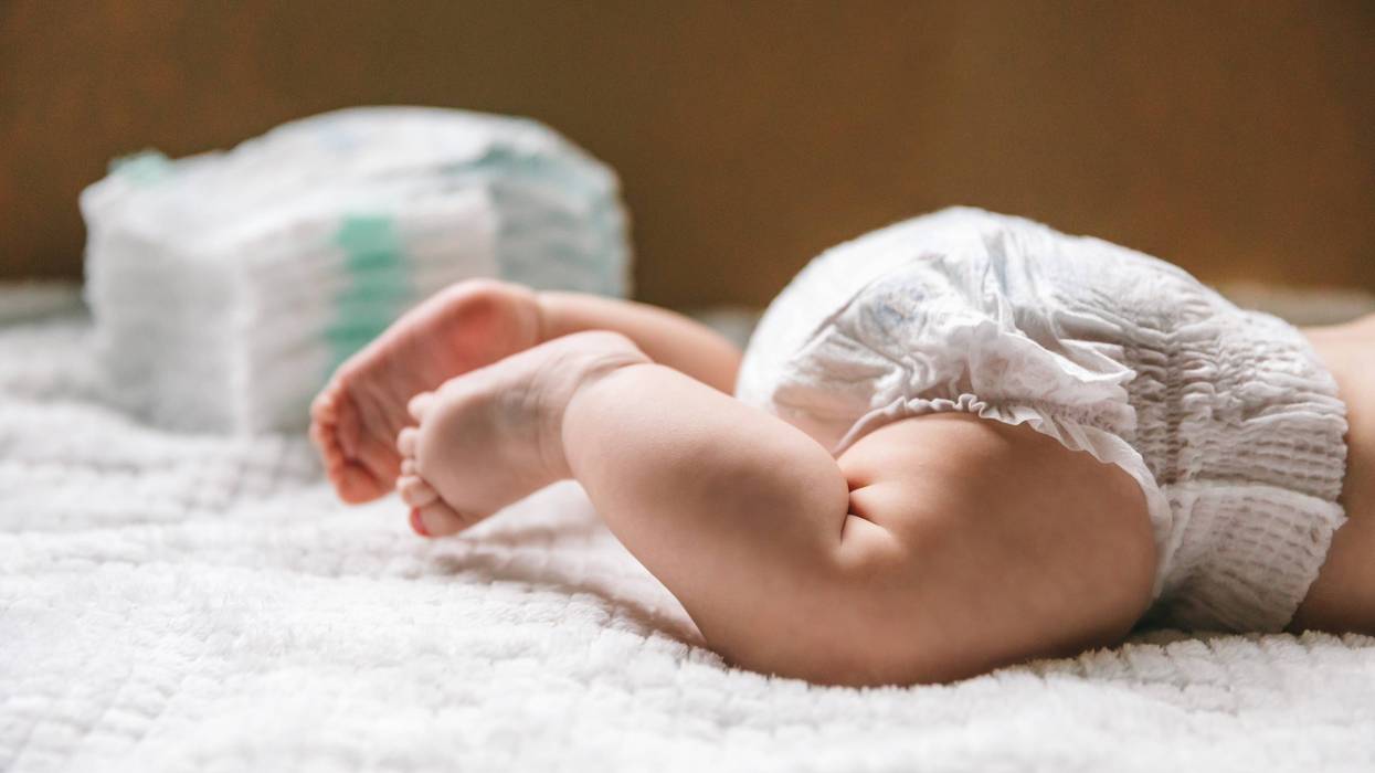 baby wearing diapers and a stack of diapers in the background