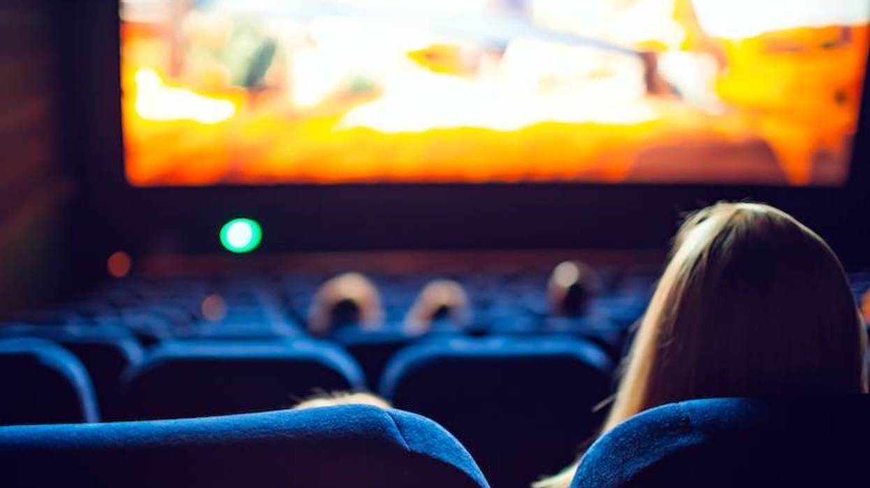 Back of a person's head watching a colorful film on a large screen in a dark movie theater.