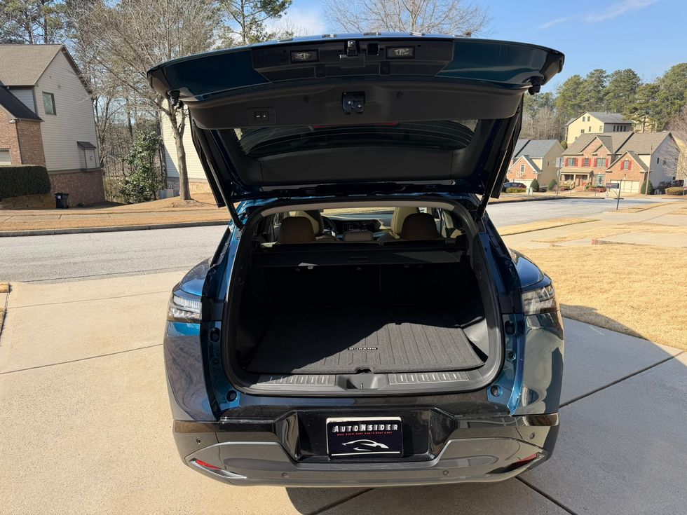 Back of a teal SUV with open trunk, revealing empty cargo space with a floor mat.