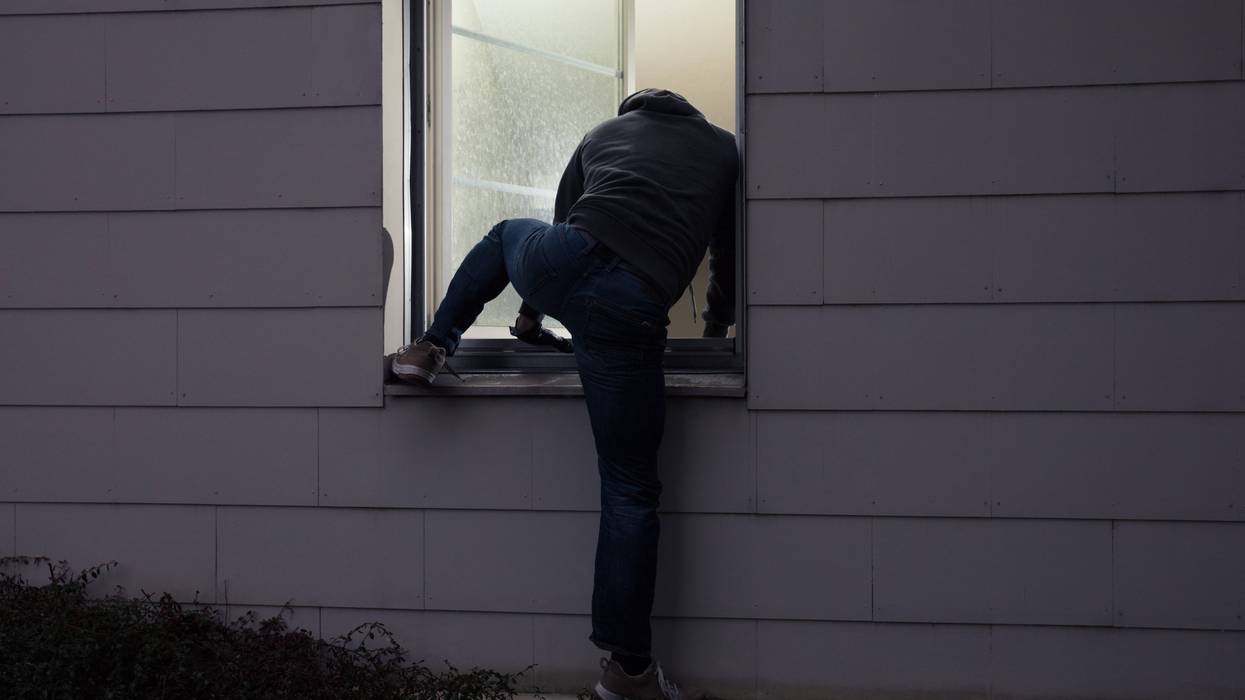 Back of man dressed in black crawling into open window