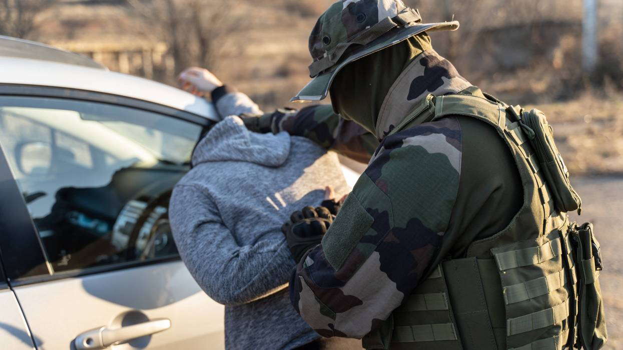 Back view of man in uniform unknown military soldier or special forces police arresting criminals illegal migrants or terrorist in sunny day at evening