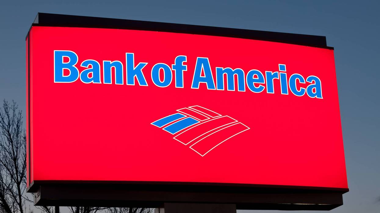 Bank of America's bright red illuminated sign with blue text and logo at dusk.