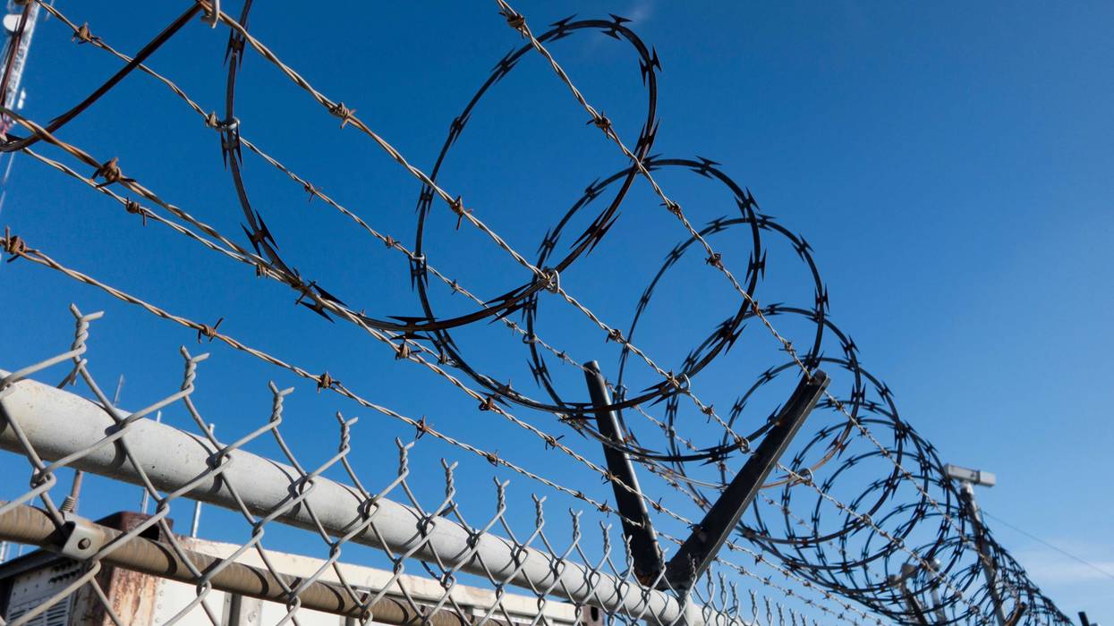 Barbed and razor wire on a fence with a security camera in the background