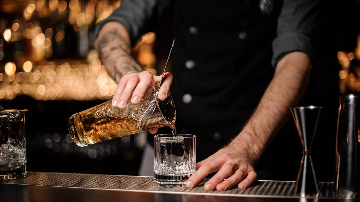 Bartender pours cocktail adding whiskey in glass