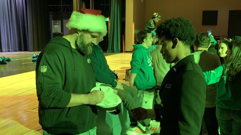 Bathed in green light, Jason Kelce signs an autograph for a student at Benjamin Franklin High School.