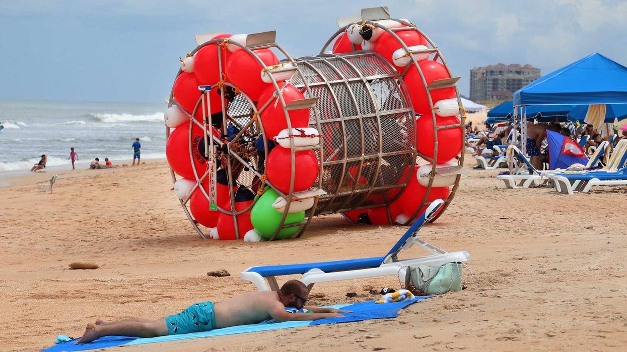 Beachgoers relax near a human-sized hamster wheel that came ashore in Daytona Beach, Florida, on July 26, 2021. The man aboard the vessel, Reza Ray Baluchi, was arrested in late August 2023 after he tried to ride across the Atlantic