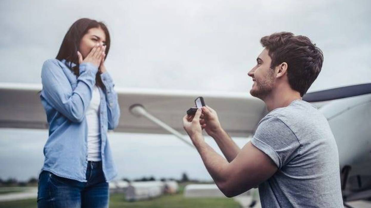 Beautiful romantic couple is standing near private plane in airport. Handsome man is making proposal to his attractive young woman.