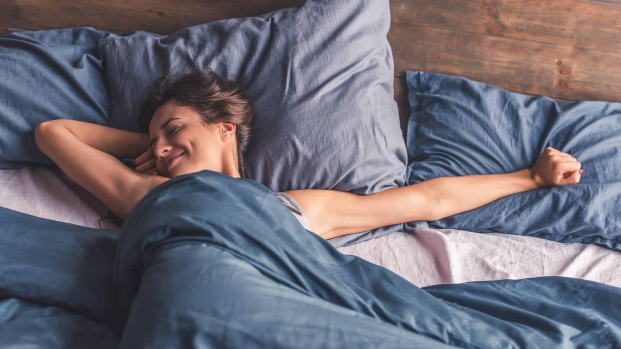 Beautiful young woman is stretching and smiling while lying in bed in the morning