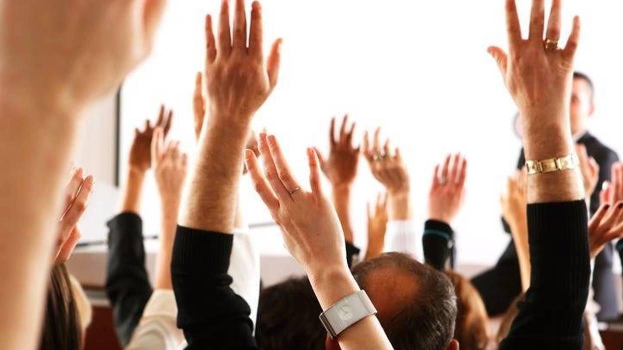 Big audience of people raising their hands to vote in favor of some topic.