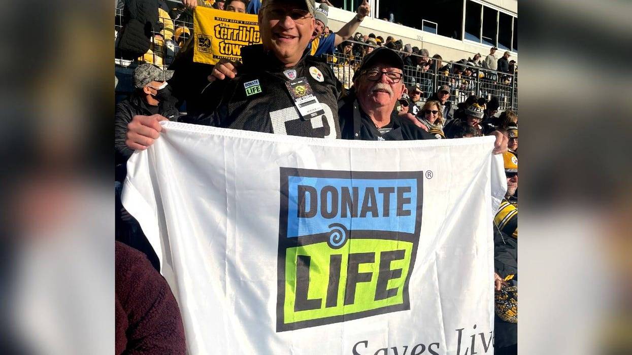 Bill Soloway and Jim Zimmerman Sr. in the stands at a Steelers game, holding a sign saying "Donate Life"