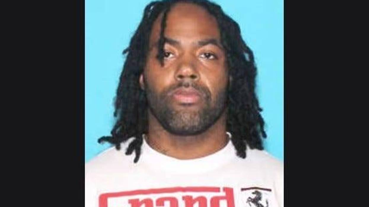 Black man in his 30s not smiling with black dreads and black facial hair wearing white t-shirt