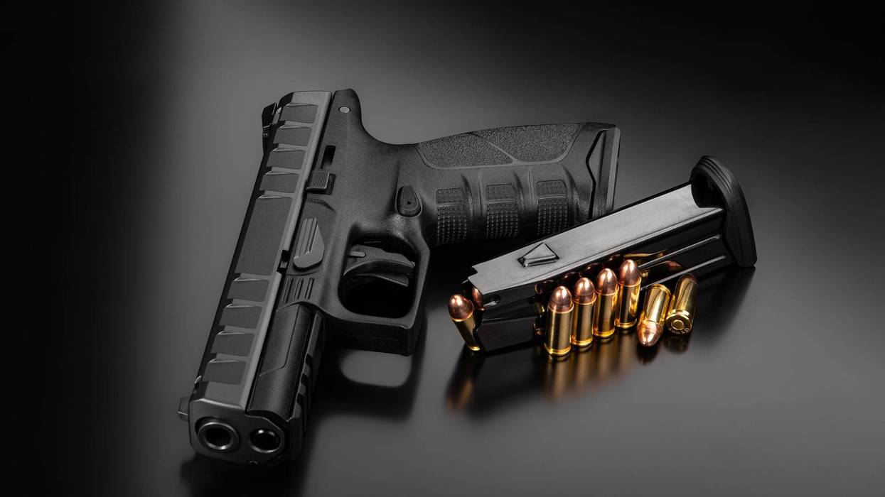 Black modern gun and ammunition for it on a dark reflective surface.