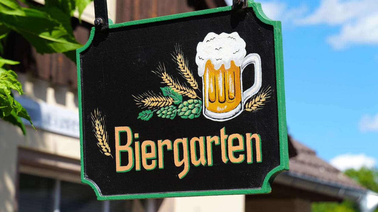 Black sign with beer mug, barley and inscription Biergarten in front of house and blue sky.