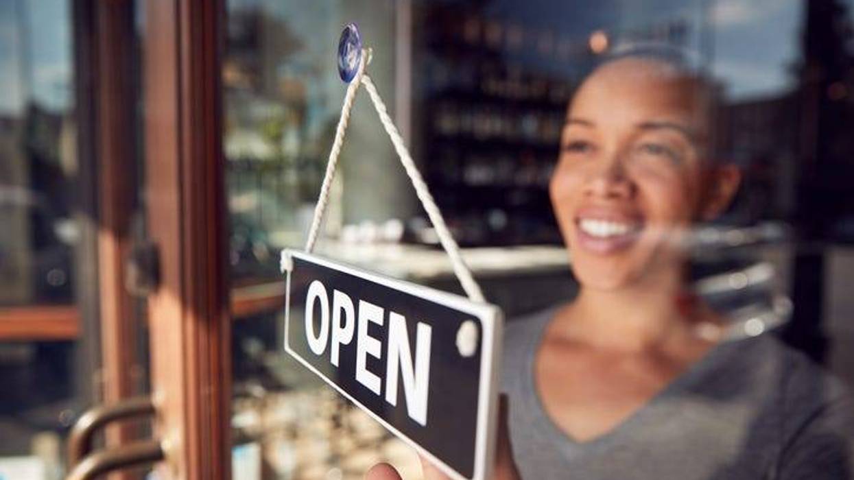 Black woman turns sign to "Open" at front of small business