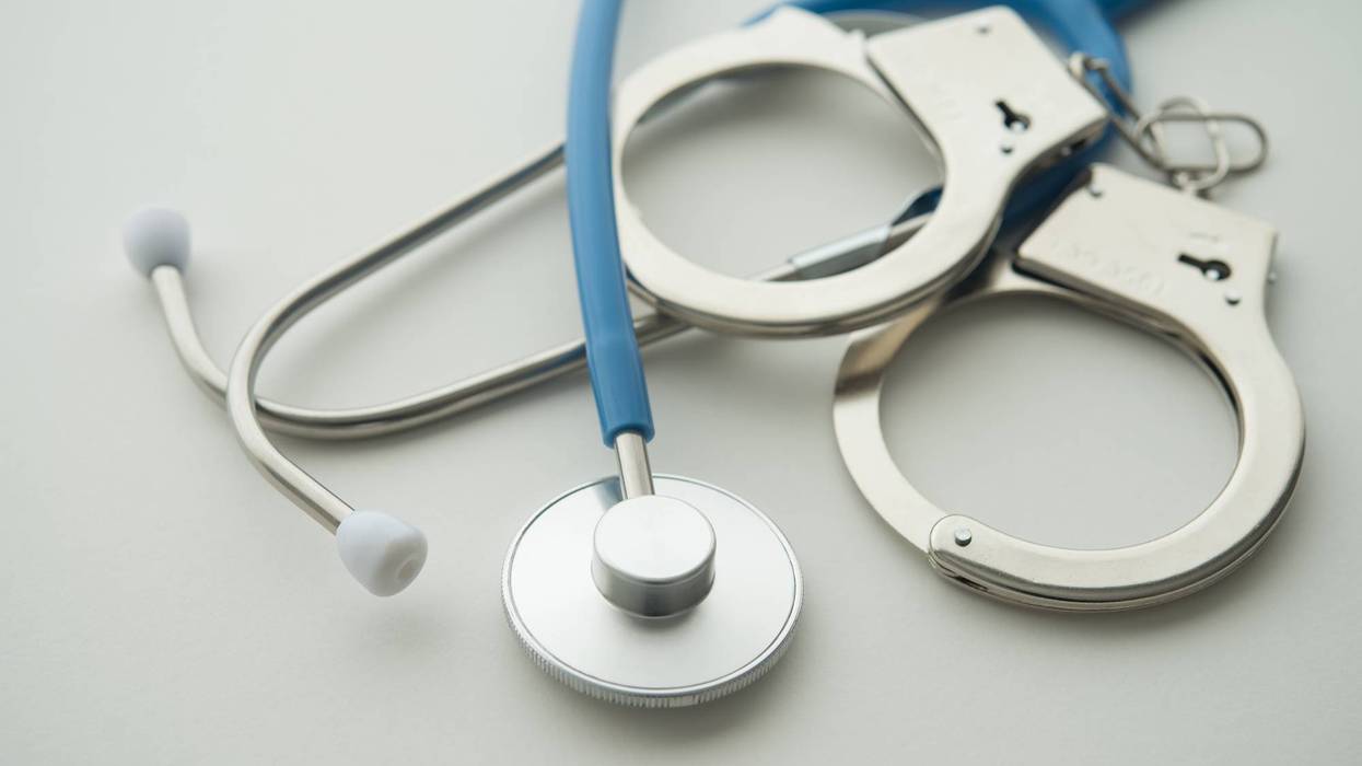 Blue stethoscope and silver handcuffs on white, representing healthcare fraud or legal issues.