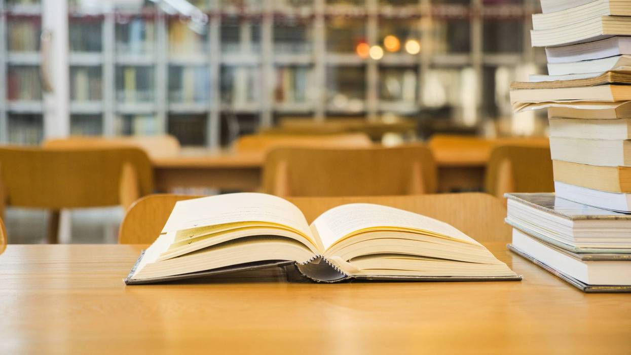 Books placed on a wooden table on blurred bookshelf in library room background