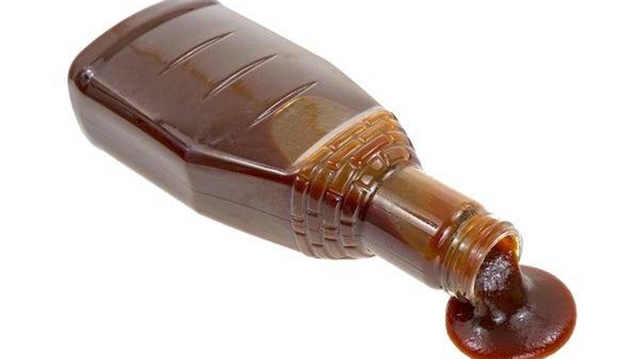 Bottle of barbecue sauce spilling on white background