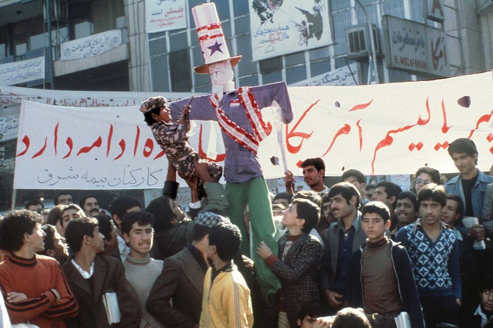 Boy in camouflage fatigues points toy pistol at an effigy of U.S. President Carter topped with empty cartoons of American-made Winston cigarettes boycotted by Iranians in the current campaign against the United States, during a demonstration outside of the U.S. Embassy, 18 November 1979. The fanatical followers of the Ayatollah Khomeini stormed the United States Embassy, 04 November 1979 in Tehran, occupied the building and took nearly 100 embassy staff and Marines hostages.