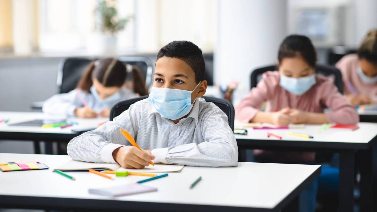 Boy in mask sitting at desk in classroom.