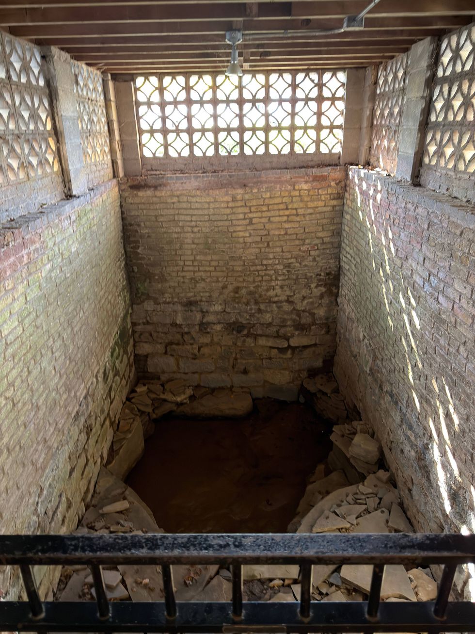 Brick-lined pit with a bed of stones and partially filled with water. Sunlight filters through patterned windows, creating a serene atmosphere.