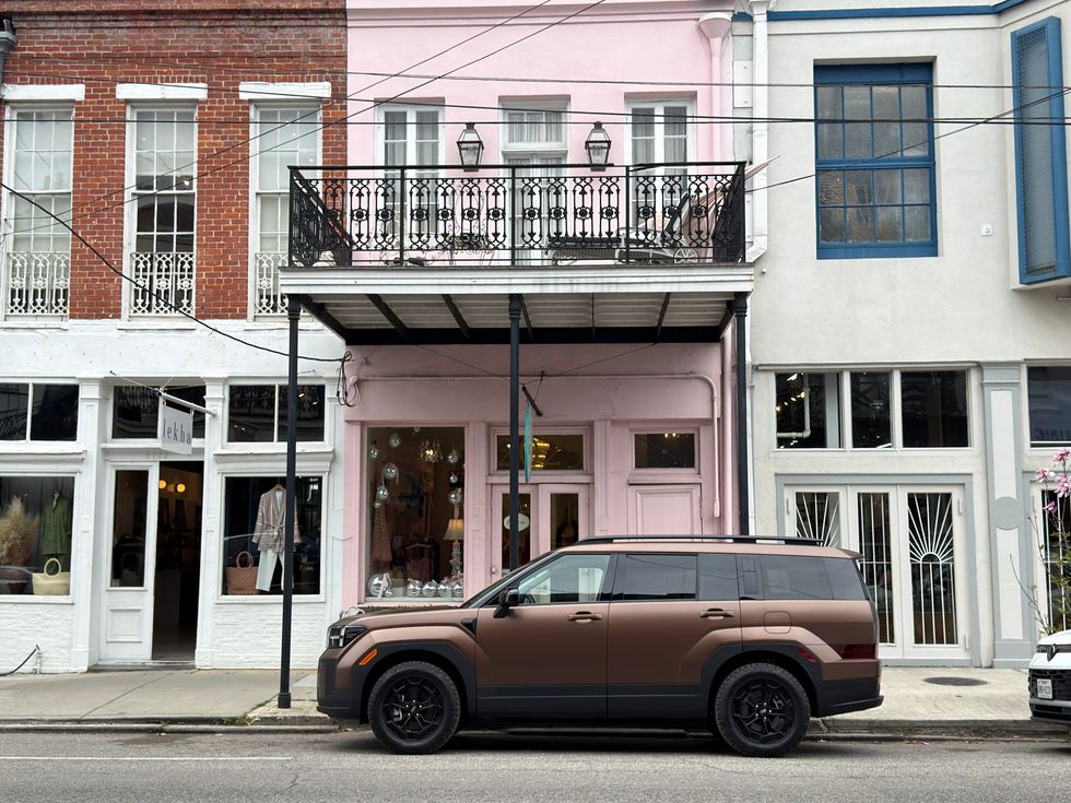 Brown SUV parked on a city street next to historic brick, pink, and white buildings with balconies.