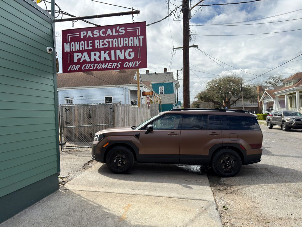 Brown SUV parked on a street under a red Pascal's Manale Restaurant parking sign.