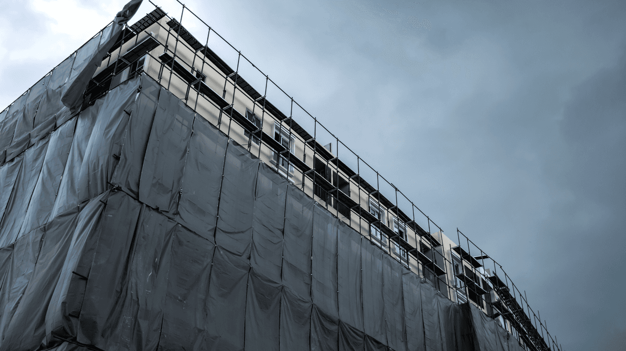 Building under construction with scaffolding and protective net is covered the building for safety and prevention dust and accidents against gray clouds before rainstorm.