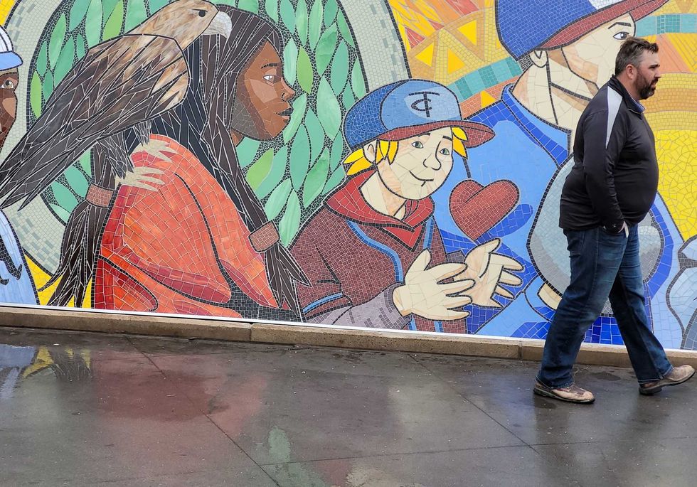 Bystander walking by "All are Welcome" mural