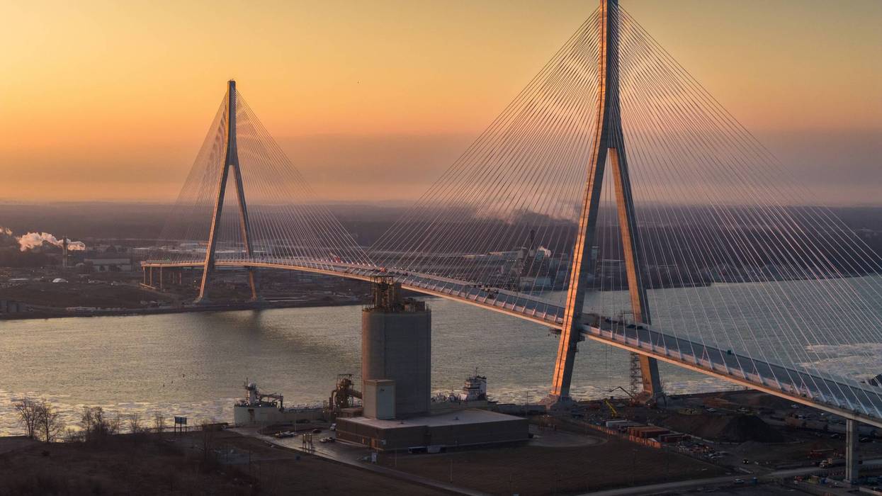 Cable-stayed bridge illuminated by golden sunset over a river, industrial area below.