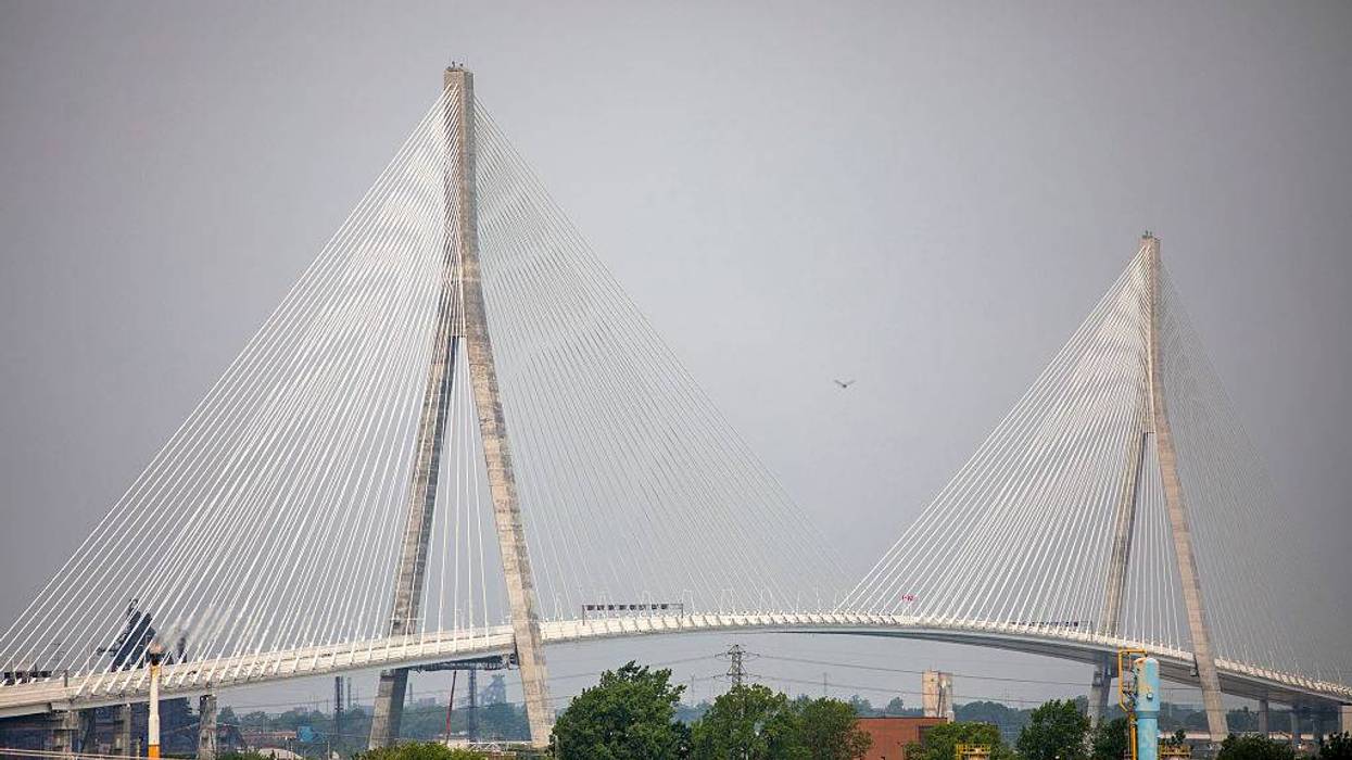 Cable-stayed bridge with two concrete towers, white cables, above a landscape and grey sky.