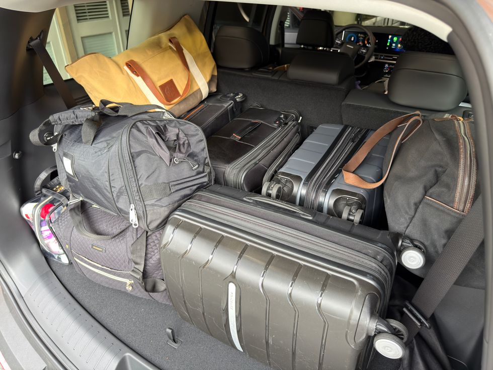 Car trunk packed with various suitcases and travel bags.