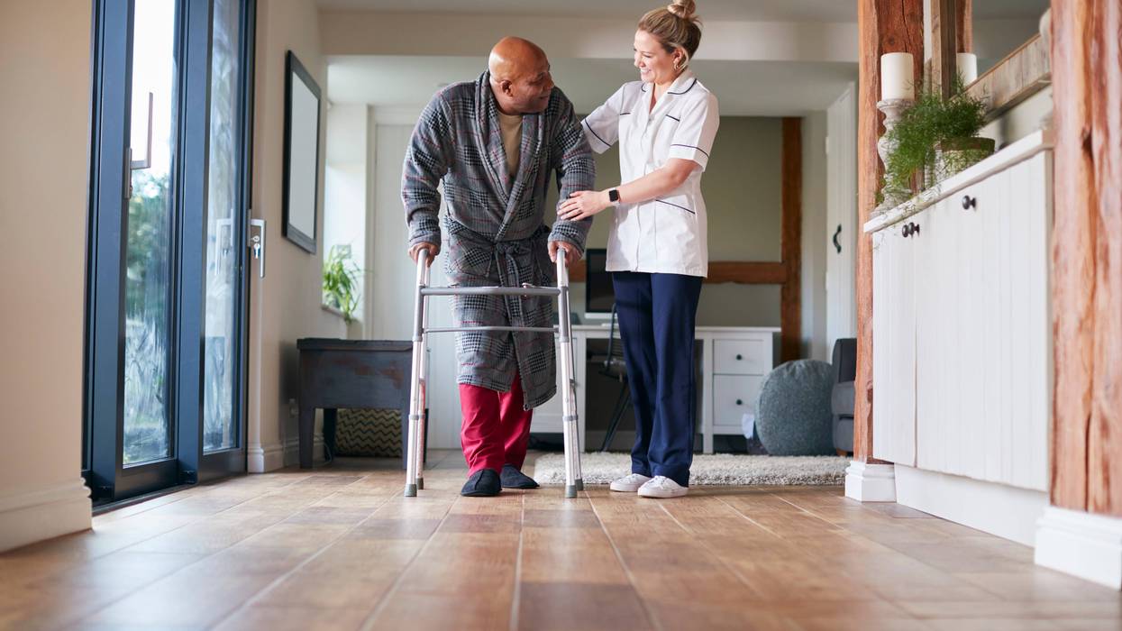 care worker helps old man with walker down hallway