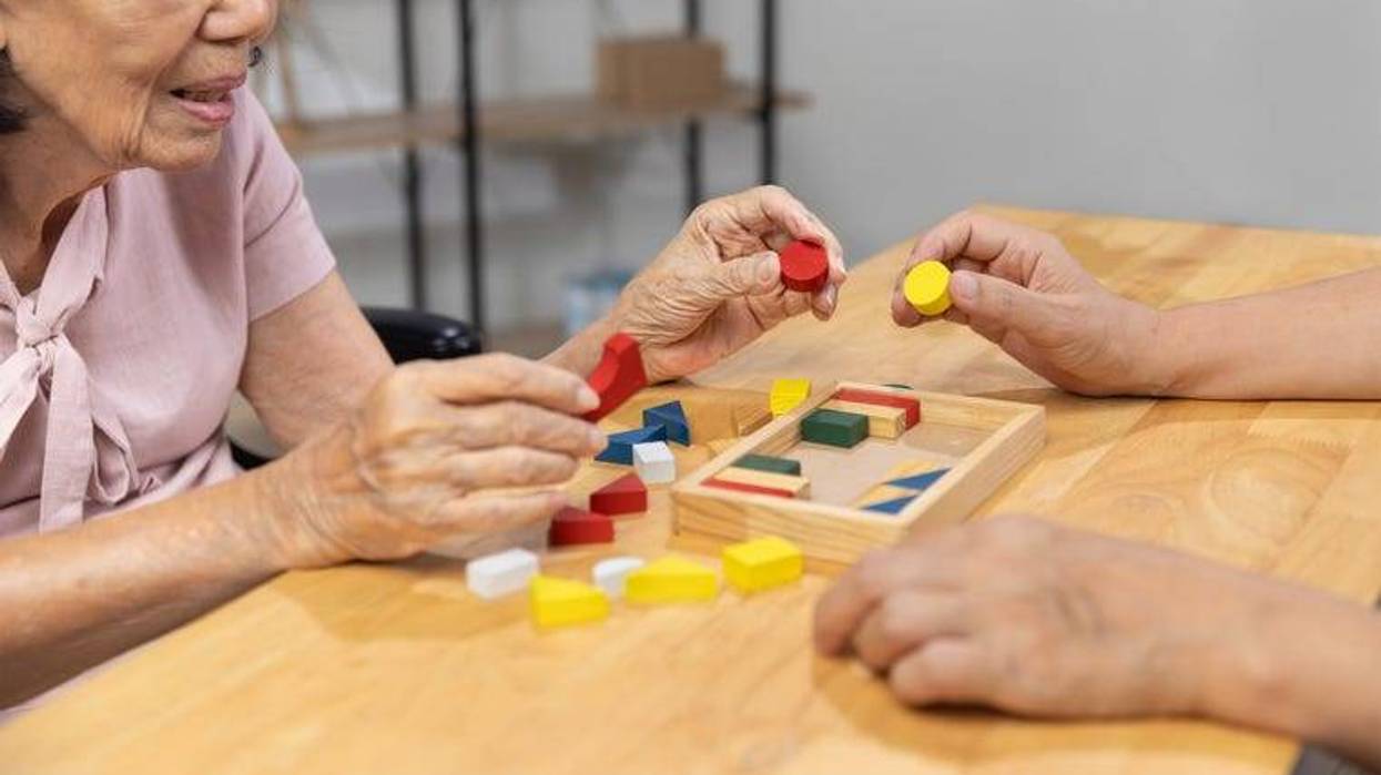 Caregiver and senior woman playing wooden shape puzzles game for dementia prevention