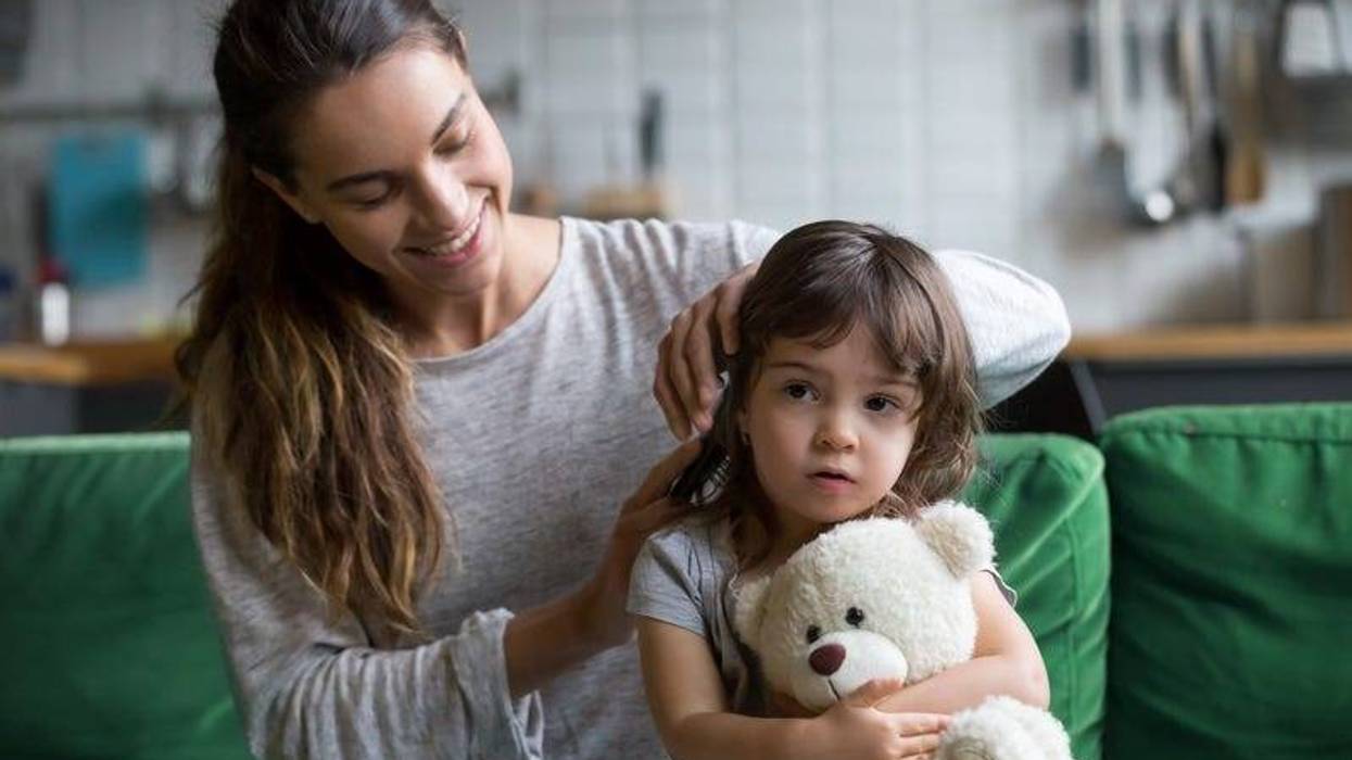Caring loving mother brushing kid daughters hair sitting on sofa.