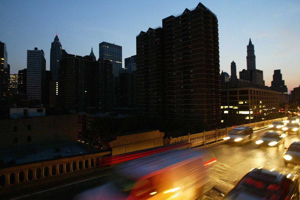 Cars head over the Brooklyn Bridge beside a blacked out New York City skyline.
