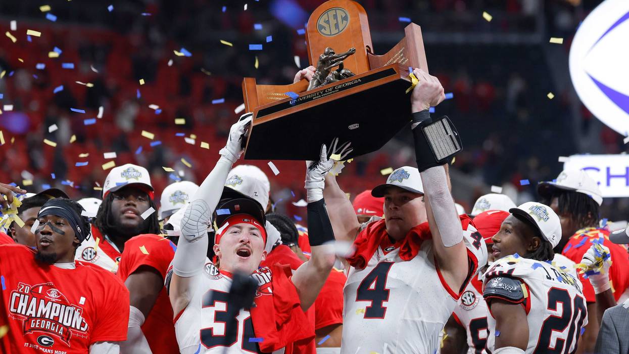 Cash Jones #32 and Oscar Delp #4 of the Georgia Bulldogs raise the 2025 SEC Championship trophy after defeating the Alabama Crimson Tide 28-7 at Mercedes-Benz Stadium.