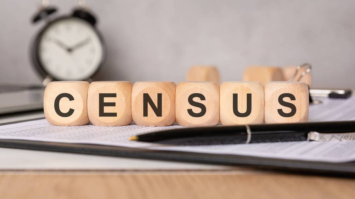 Census concept with wooden blocks on documents, pen, and clock in the background.
